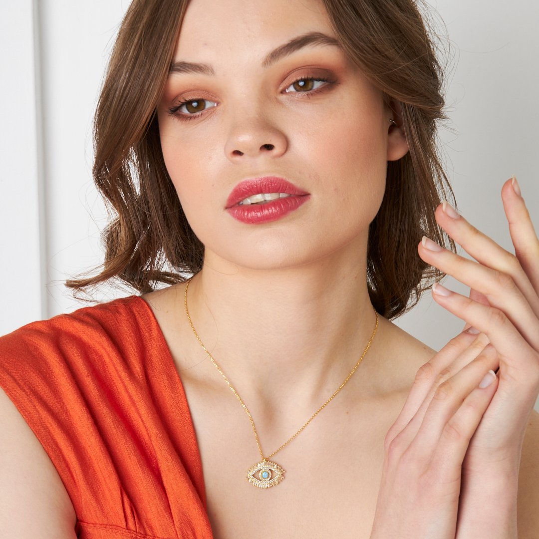 14K gold Augen Halskette mit Baguettesteinen, elegant präsentiert von einer Frau mit rotem Oberteil.